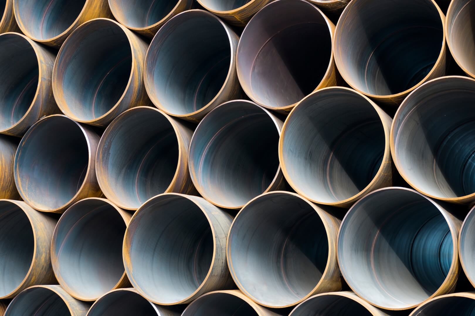 Close-up view of stacked cylindrical metal pipes arranged in a grid, showing dark hollow interiors and lighted rims creating a repeating circular pattern.